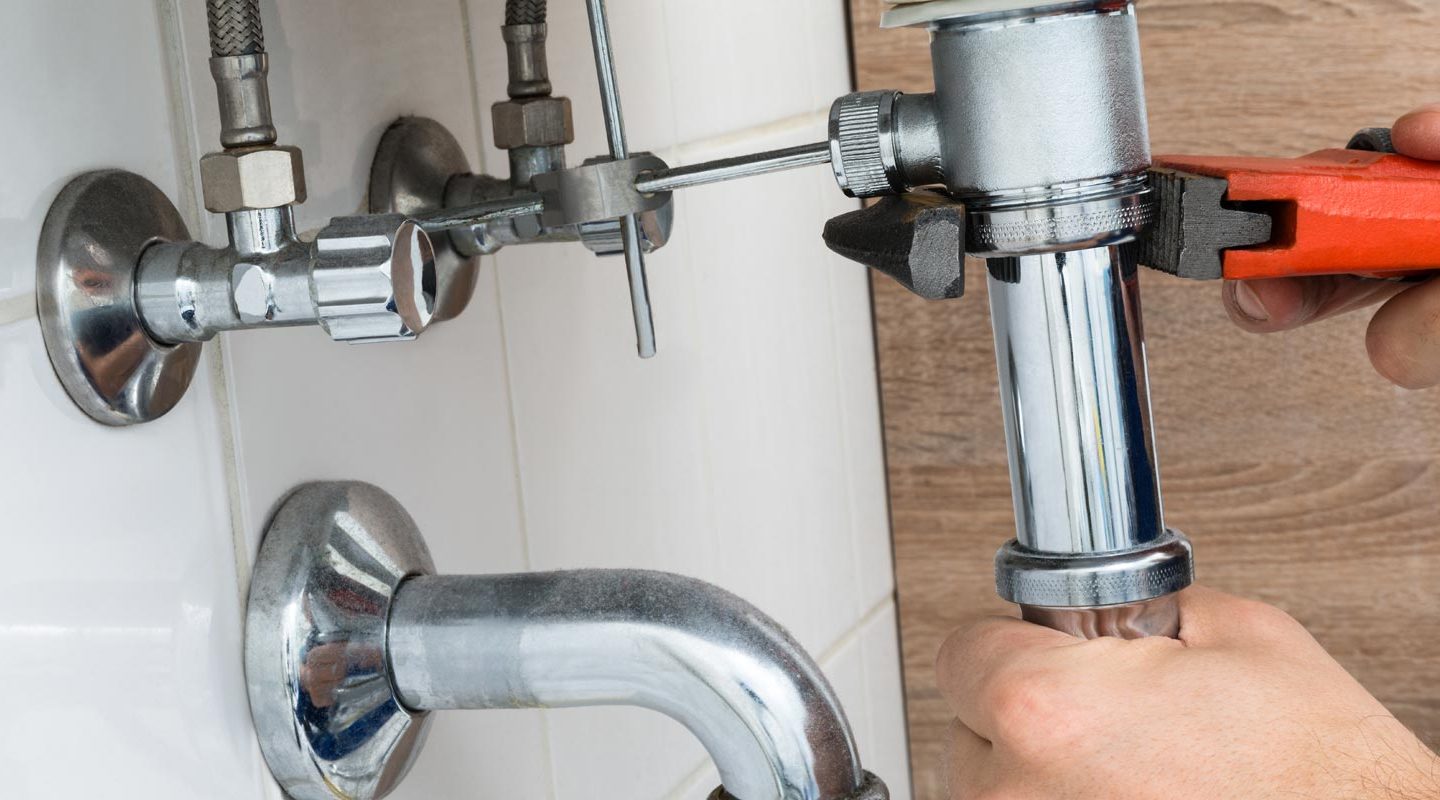 a man using a wrench on the outlet pipe of a sink