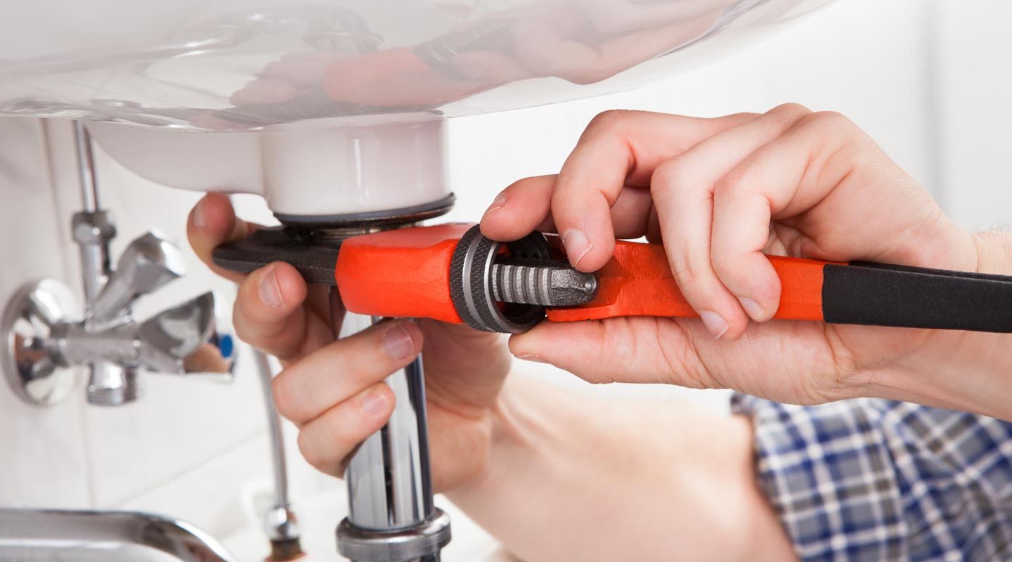 a man using a wrench on the outlet pipe of a sink