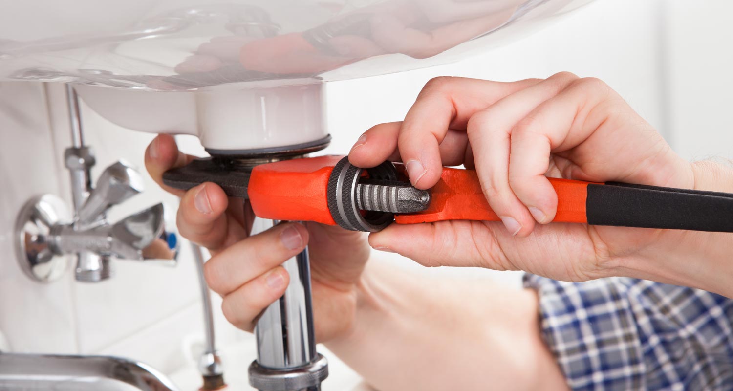 a man using a wrench on the outlet pipe of a sink