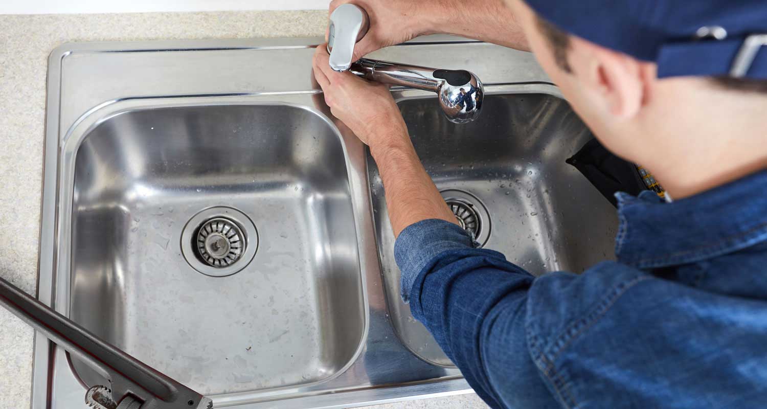 a man fixing a sink in a kitchen